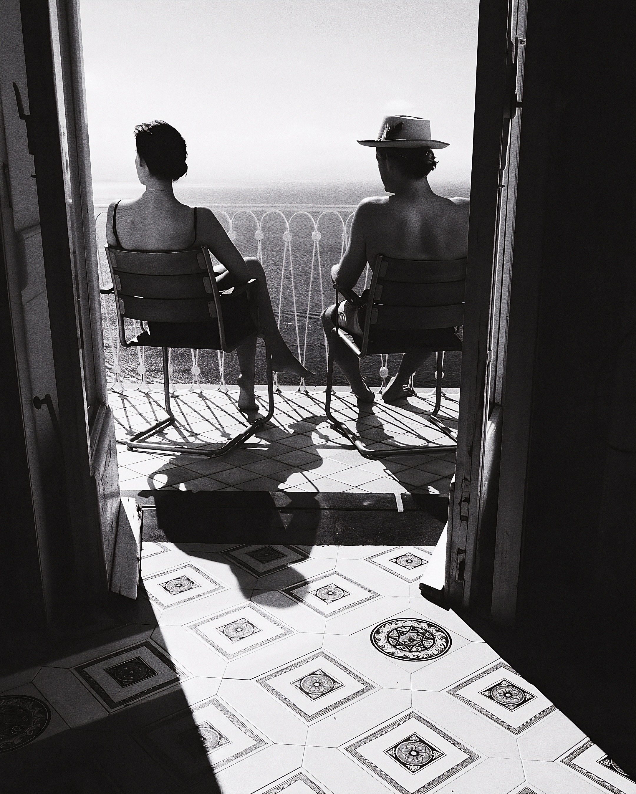 Two people relaxing on a sunlit balcony overlooking the sea